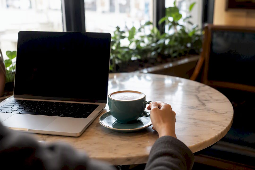Hand reaching for coffee next to laptop